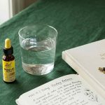 A small Rescue Remedy dropper bottle beside a glass of water and a journal in soft natural light