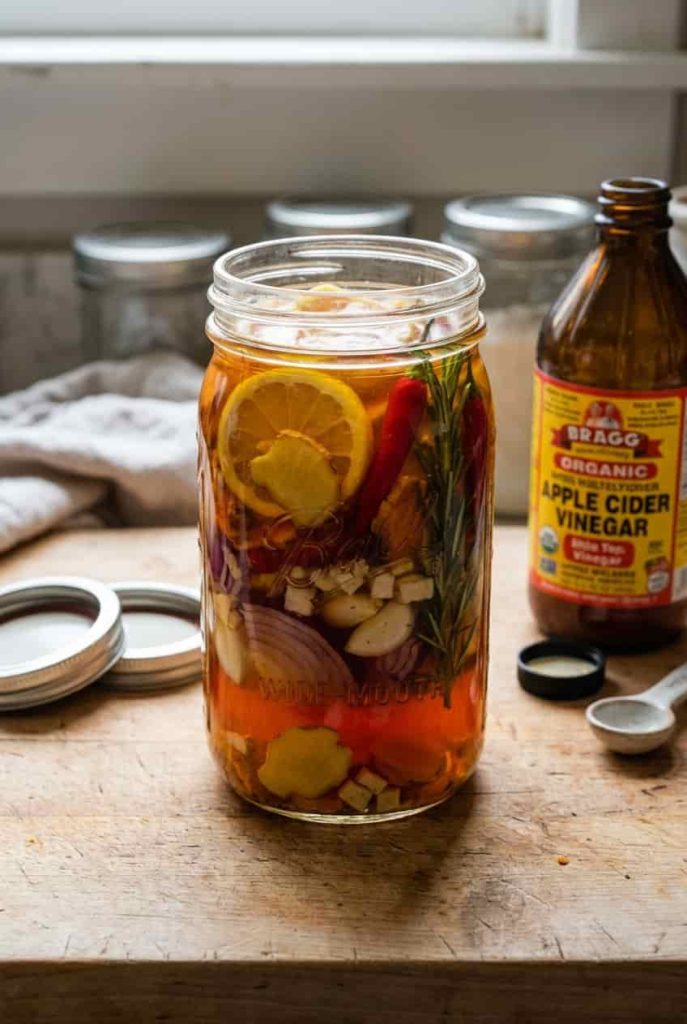 A glass jar of homemade fire cider with garlic, ginger, turmeric, chili peppers, horseradish, lemon, and rosemary
